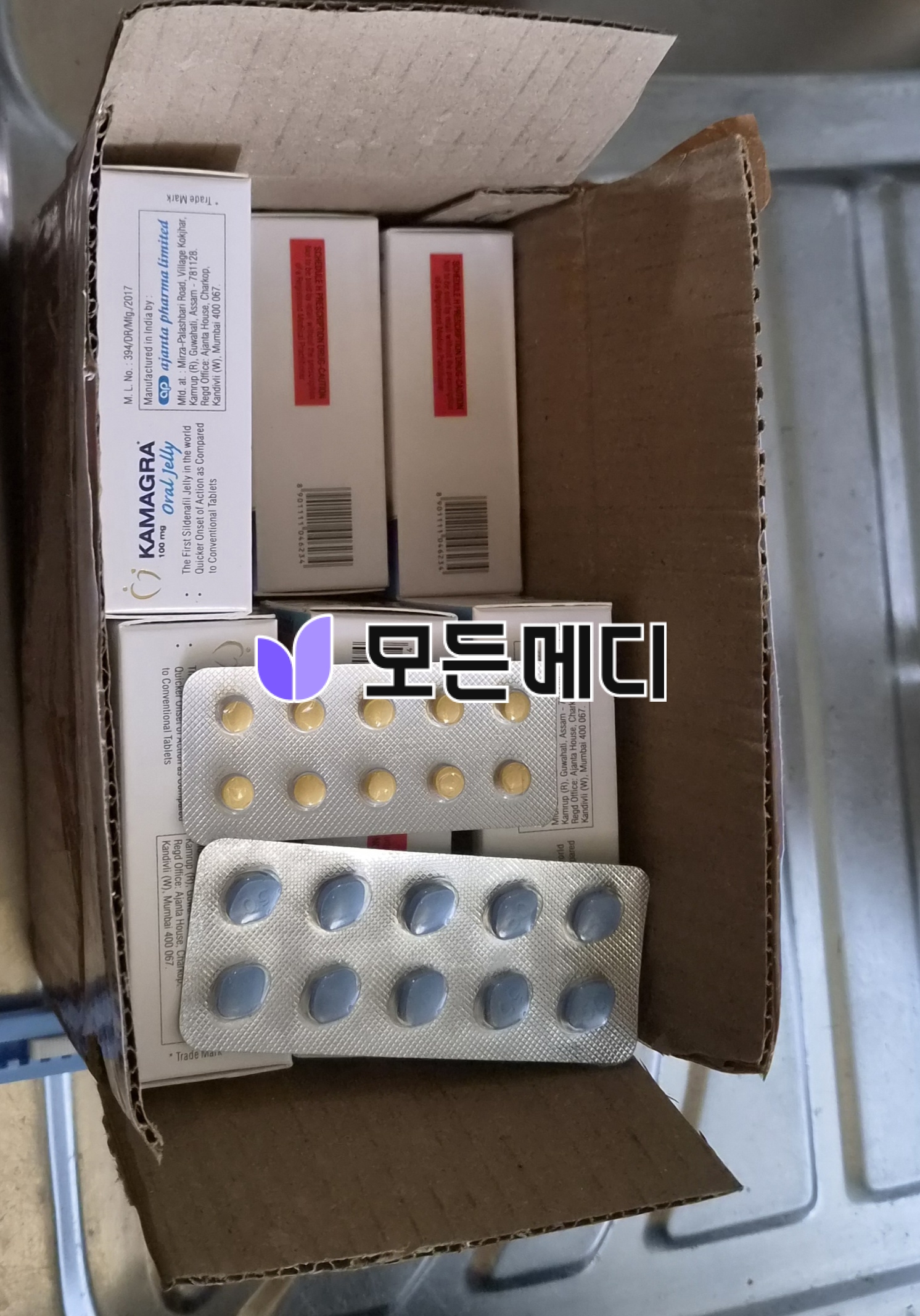 Box with blister packs of pale yellow pills and white labeled boxes inside, likely medicine bottles held in a cardboard carton.